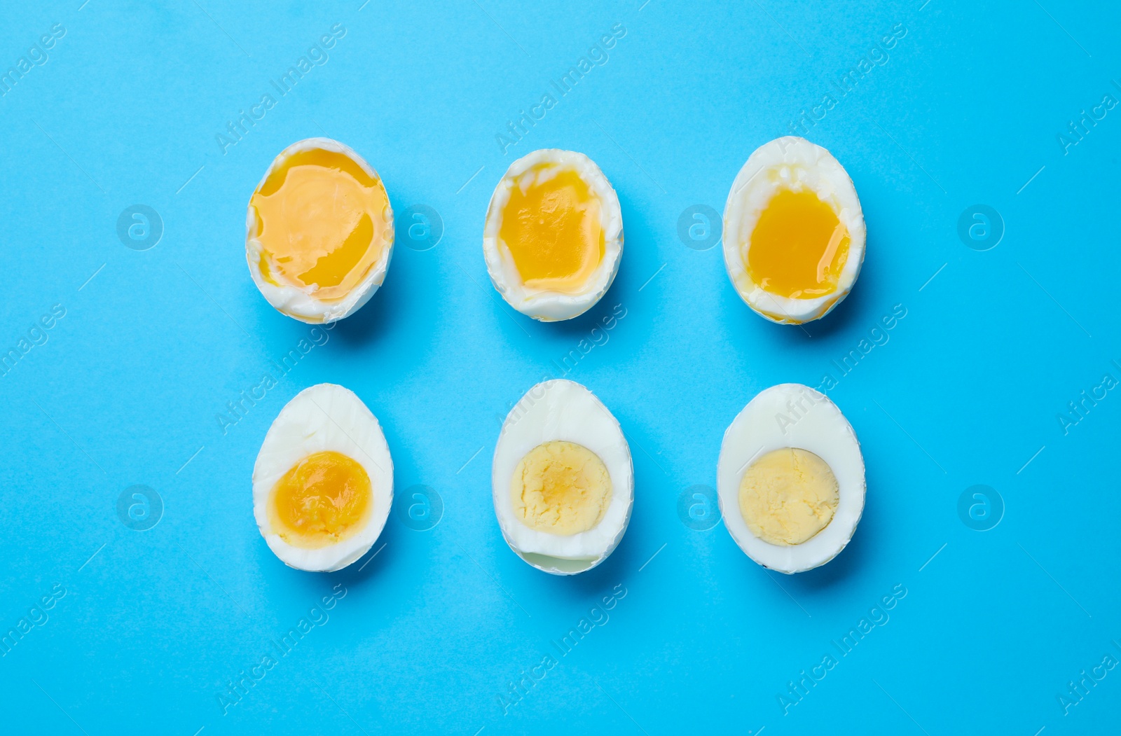 Photo of Different readiness stages of boiled chicken eggs on light blue background, flat lay