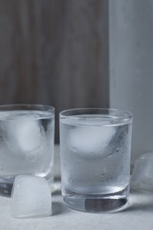 Photo of Shot glasses of vodka with ice cubes on light grey table