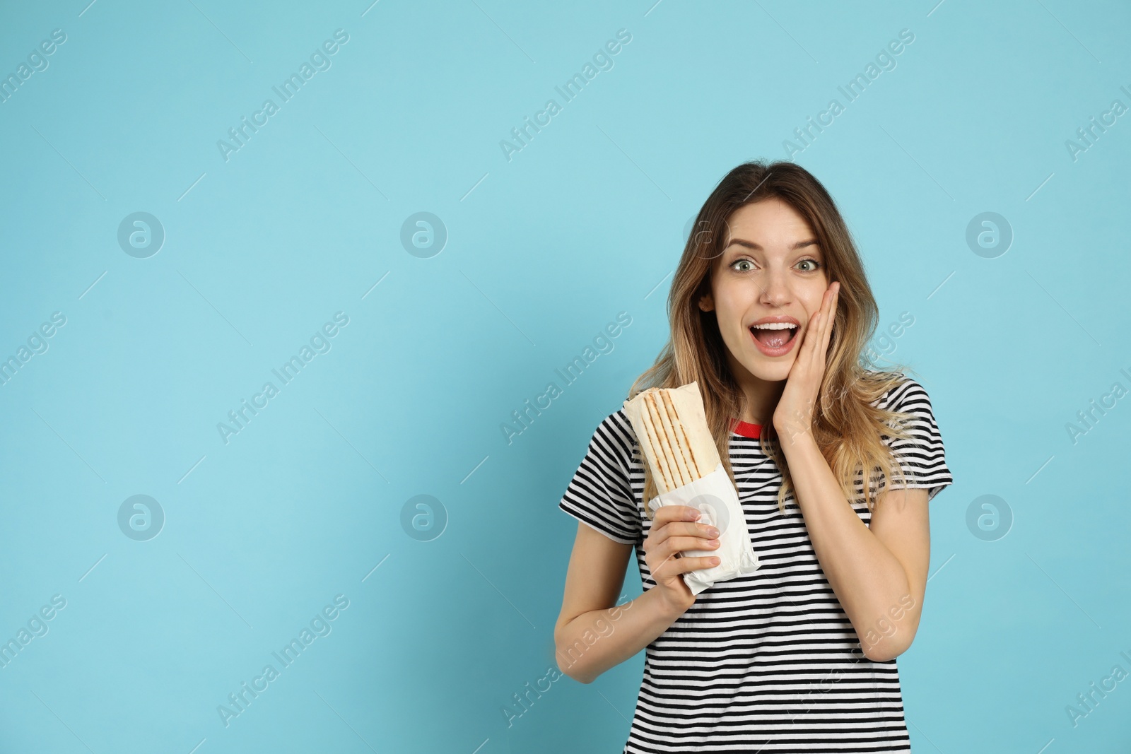 Photo of Emotional young woman with delicious shawarma on turquoise background, space for text