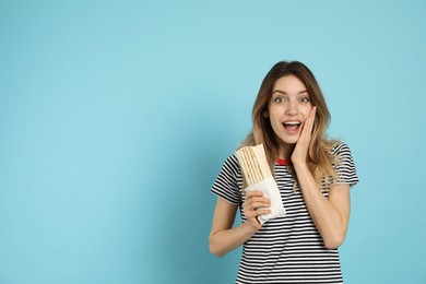 Emotional young woman with delicious shawarma on turquoise background, space for text