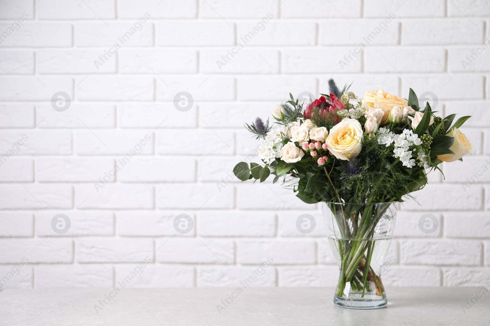 Photo of Beautiful bouquet with roses on grey table against white brick wall, space for text