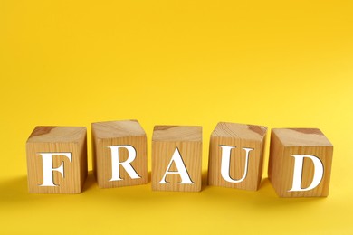 Photo of Wooden cubes with word Fraud on yellow background, space for text