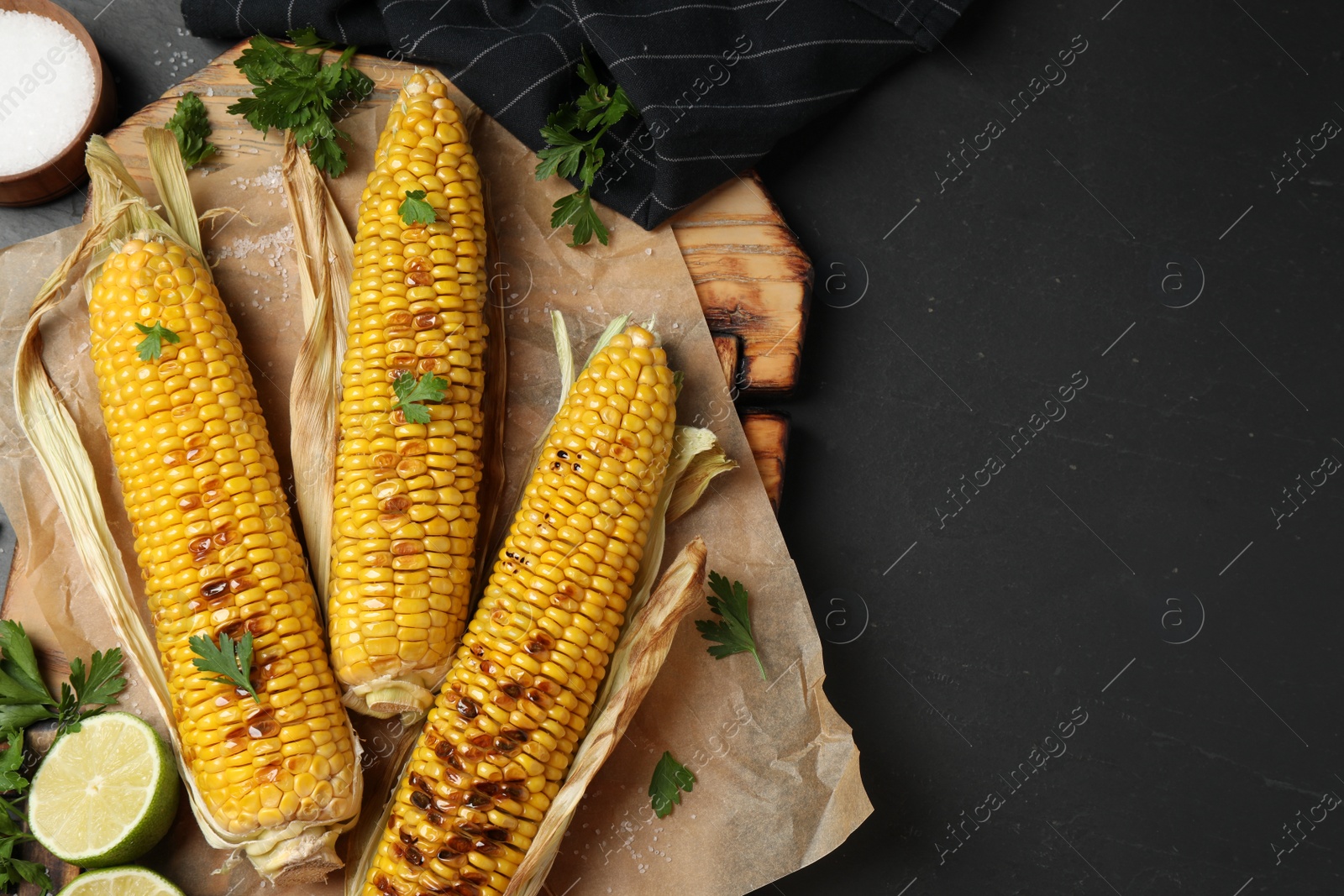 Photo of Tasty grilled corn on black table, flat lay. Space for text