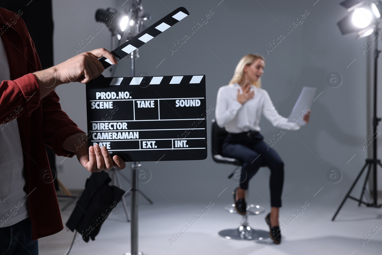 Photo of Casting call. Emotional woman performing while second assistance camera holding clapperboard against grey background in studio, selective focus