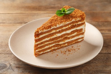 Photo of Slice of delicious layered honey cake with mint on wooden table