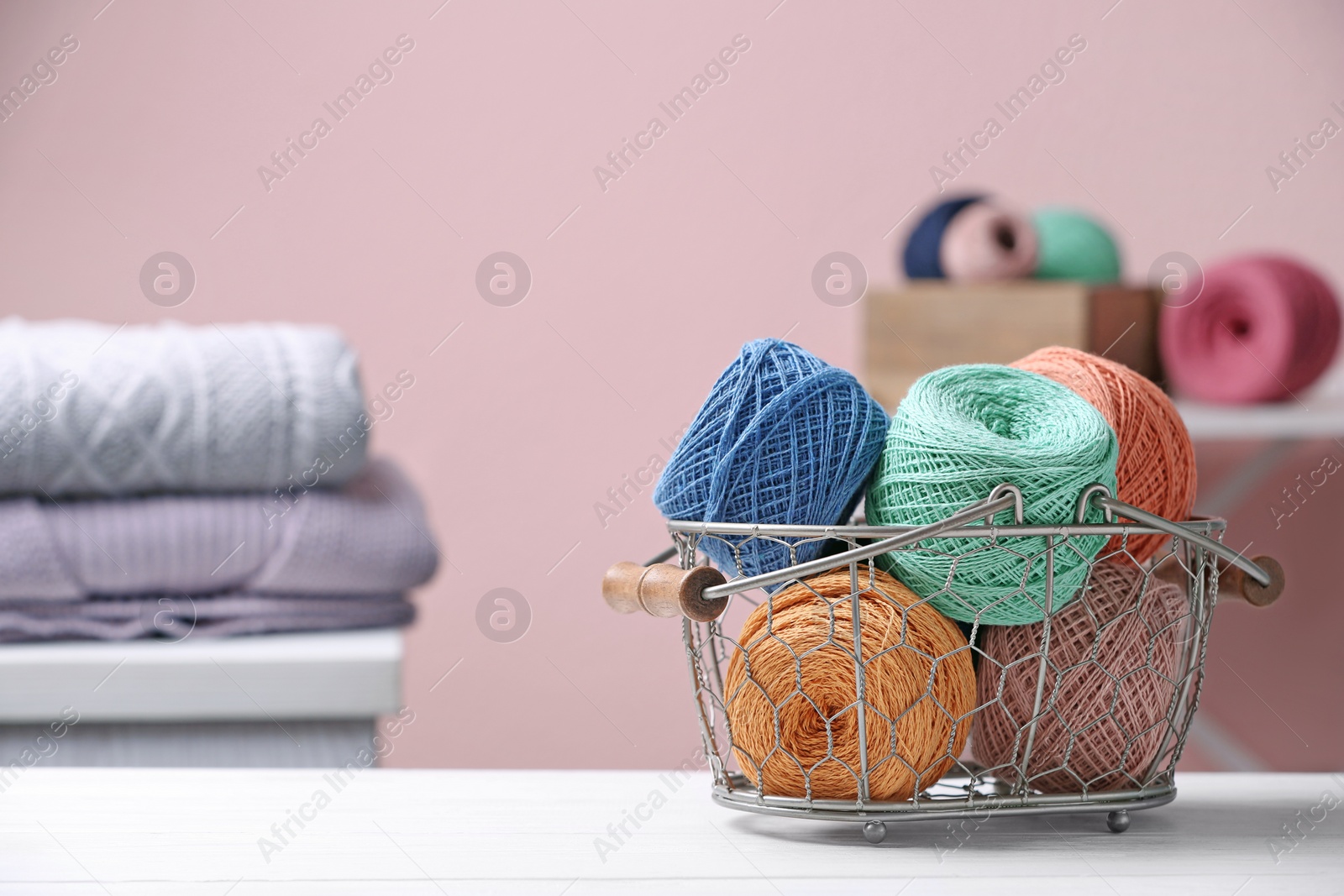 Photo of Colorful clews of threads in basket on table against blurred background, space for text