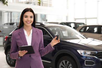 Photo of Saleswoman with key and clipboard in car salon
