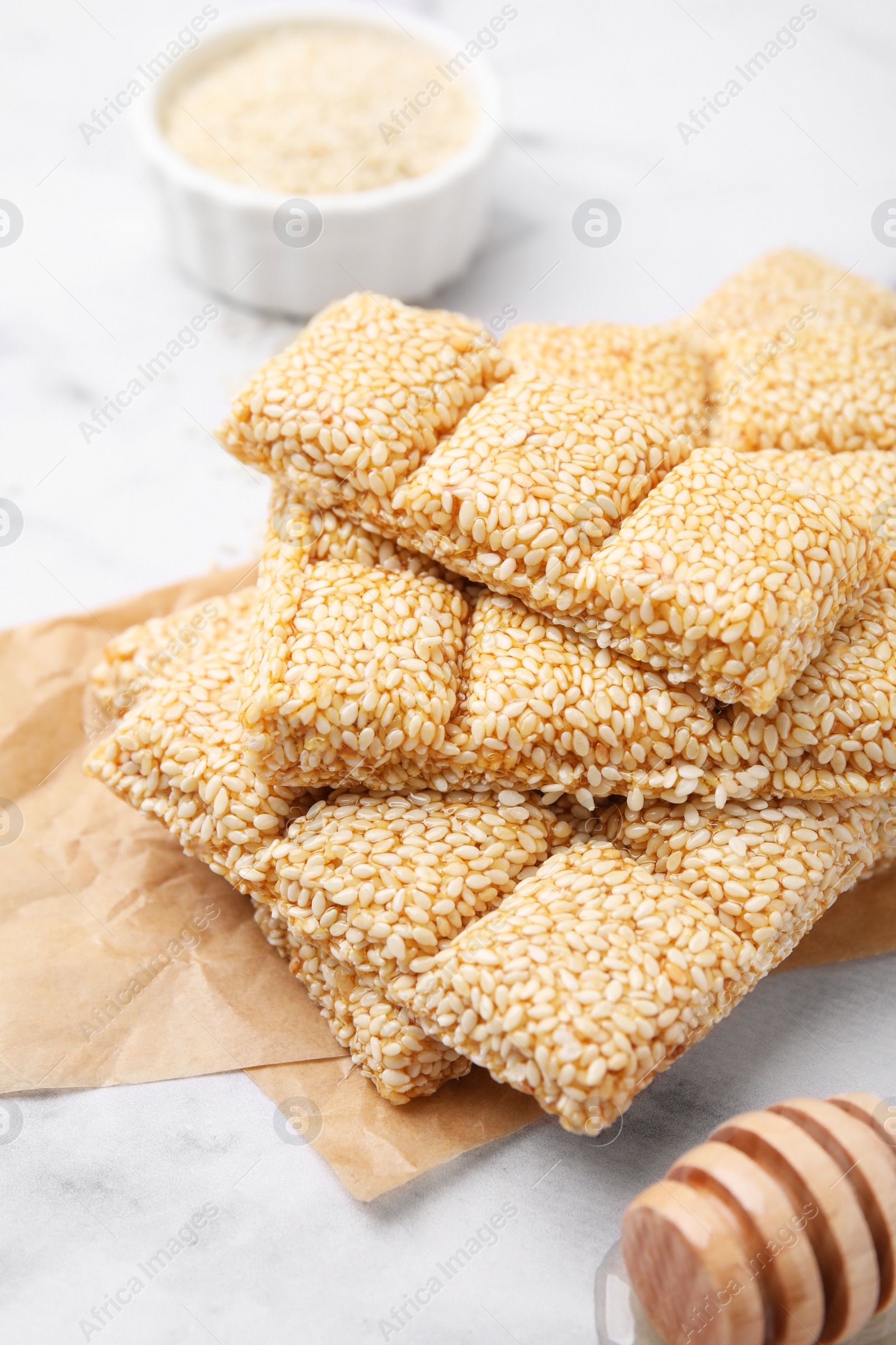 Photo of Delicious sweet kozinaki bars, sesame seeds and wooden dipper on white marble table, closeup