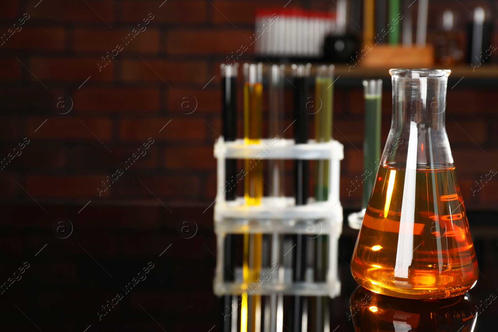 Photo of Laboratory glassware with different types of oil on black mirror table indoors, closeup. Space for text