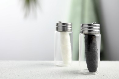 Biodegradable dental flosses in glass jars on white table, closeup. Space for text