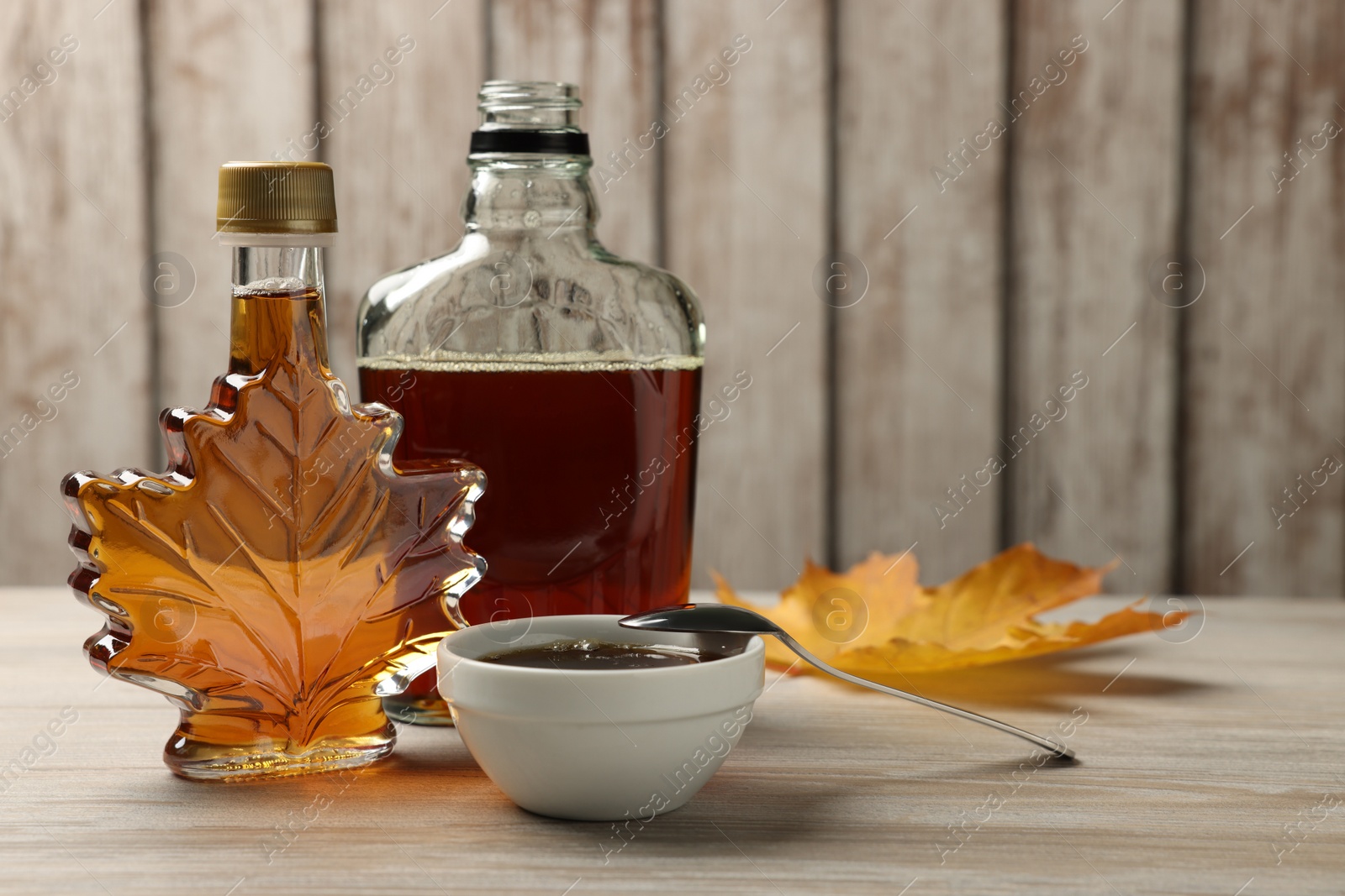 Photo of Bottles and bowl of tasty maple syrup on wooden table, space for text