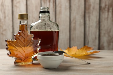 Bottles and bowl of tasty maple syrup on wooden table, space for text