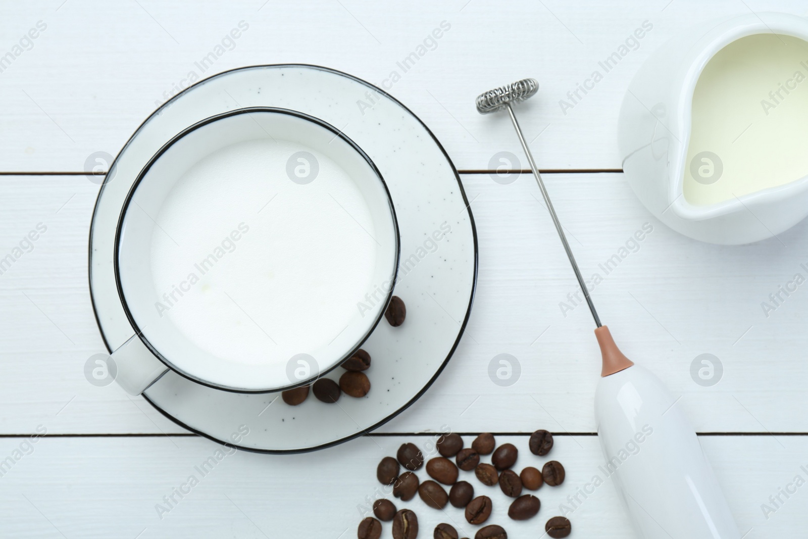 Photo of Flat lay composition with mini mixer (milk frother), whipped milk and coffee beans on white wooden table