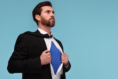 Photo of Confident businessman wearing superhero costume under suit on light blue background. Space for text