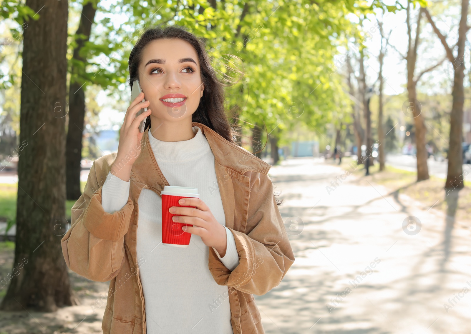 Photo of Young woman talking by phone outdoors on sunny day