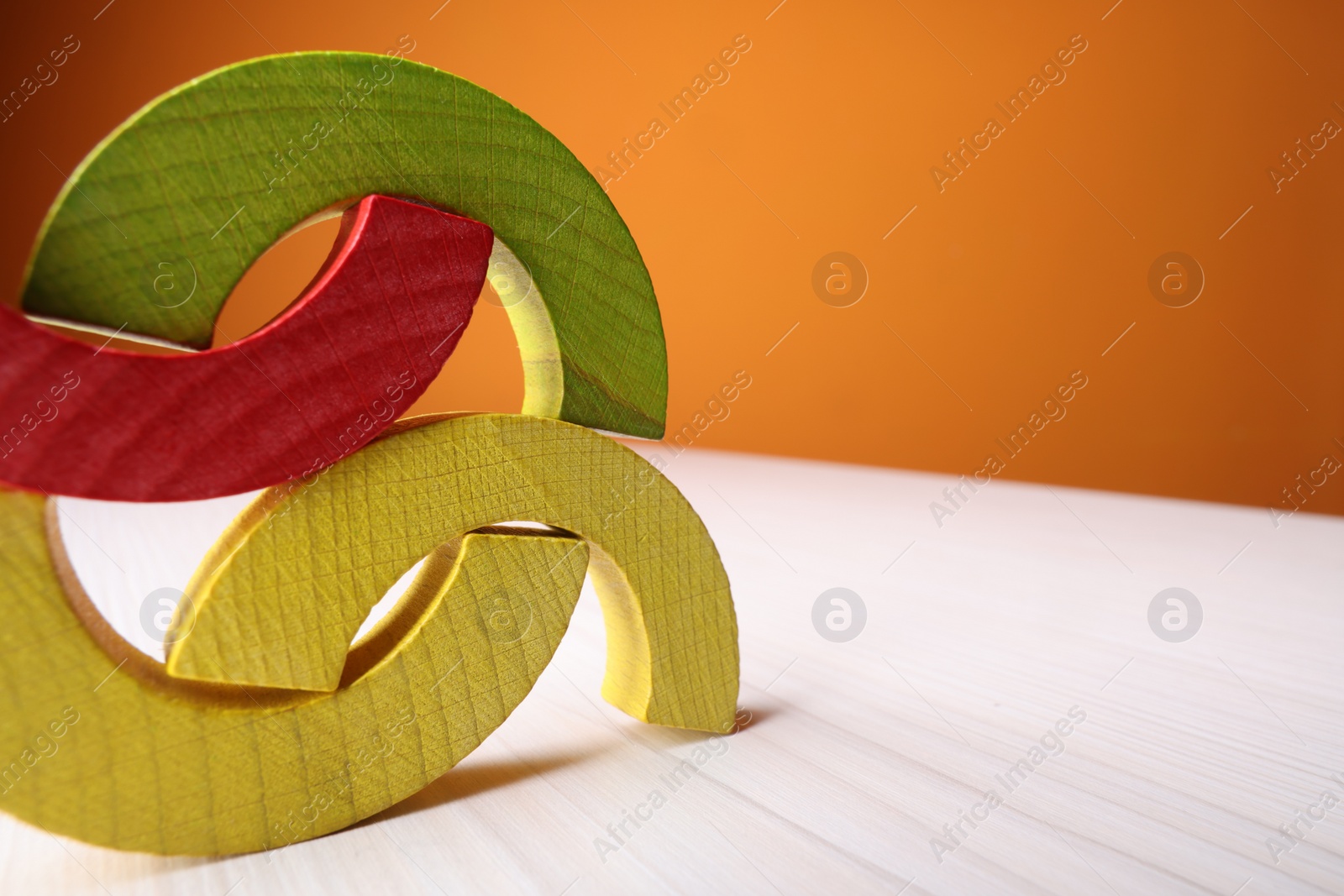 Photo of Colorful wooden pieces of educational toy on light table against orange wall, closeup and space for text. Motor skills development