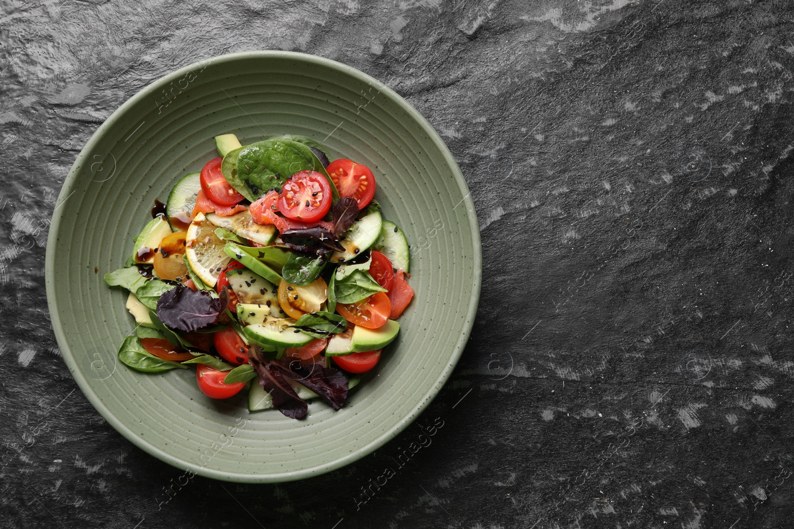 Photo of Delicious vegetable salad on black textured table, top view. Space for text