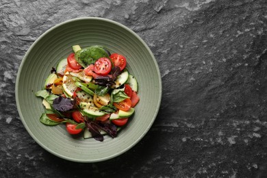 Photo of Delicious vegetable salad on black textured table, top view. Space for text