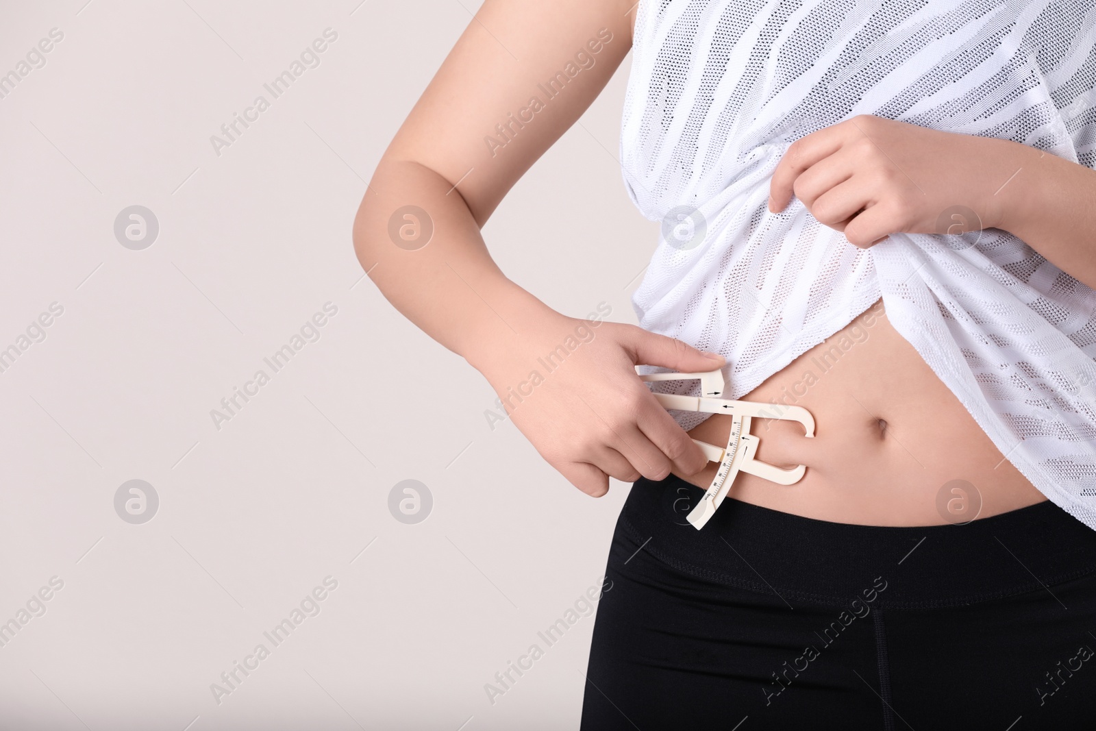 Photo of Young woman measuring body fat with caliper on beige background, closeup. Nutritionist's tool