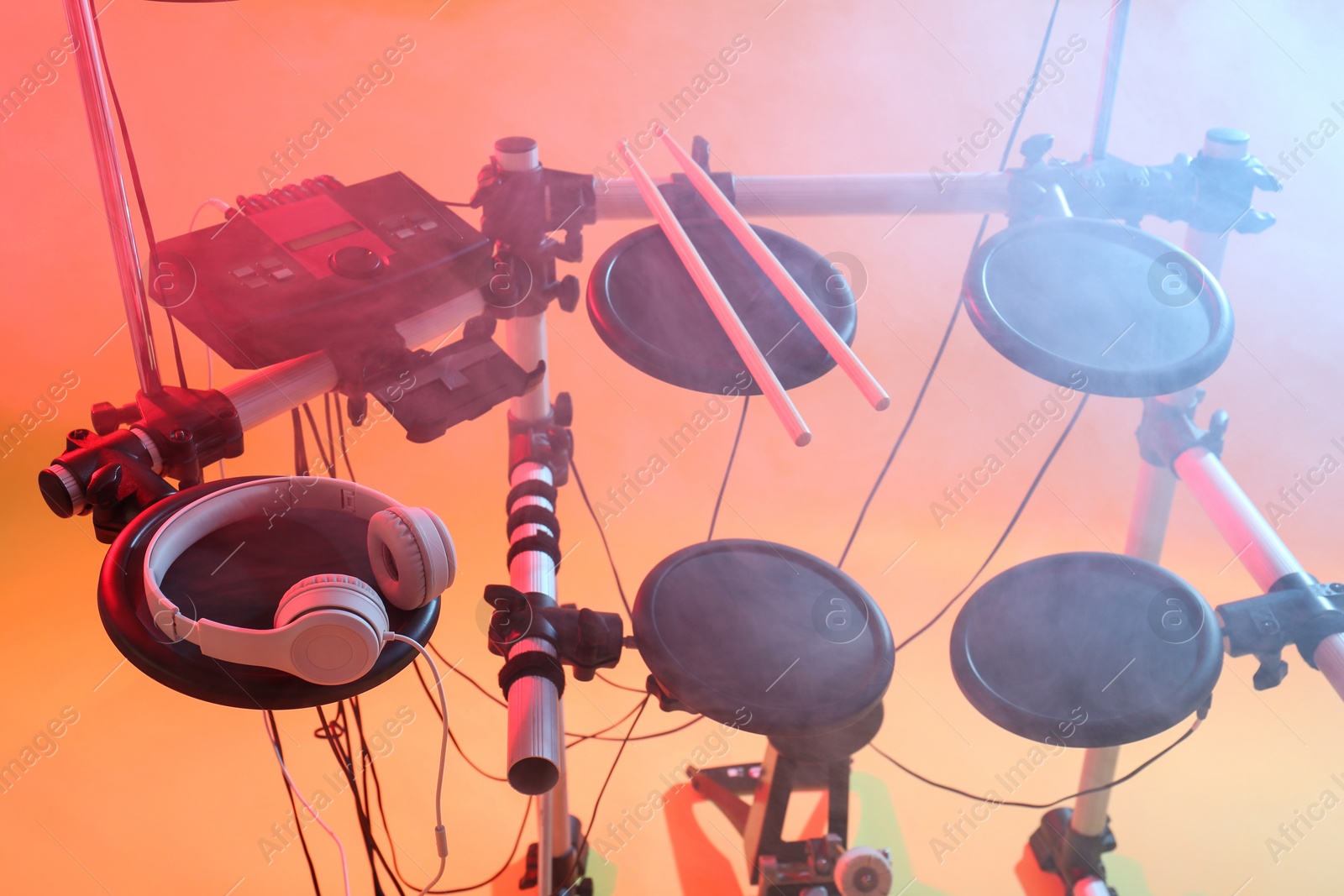 Photo of Modern electronic drum kit and smoke on orange background, color toned. Musical instrument