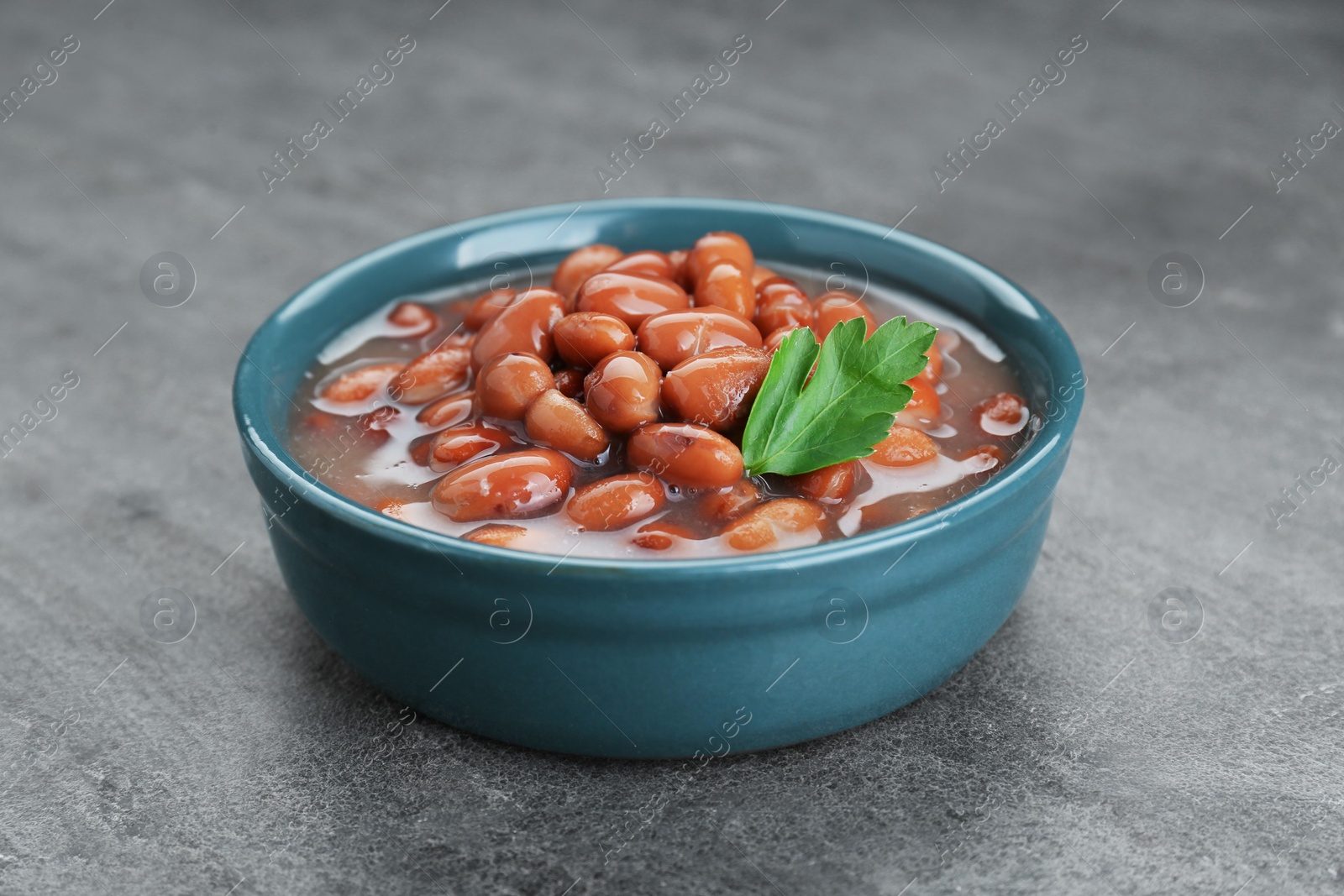 Photo of Bowl of canned kidney beans with parsley on grey table, closeup