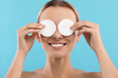 Photo of Smiling woman removing makeup with cotton pads on light blue background