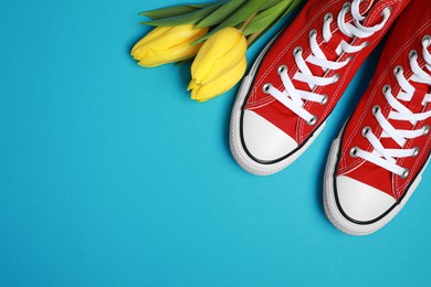Photo of Pair of new stylish red sneakers and beautiful tulips on light blue background, flat lay. Space for text