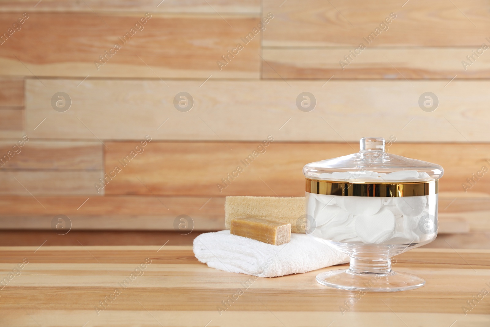 Photo of Decorative glass jar with cotton pads and bathroom accessories on table against wooden background. Space for text