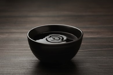 Photo of Black bowl with water on dark wooden table