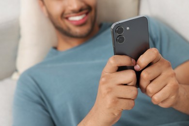 Man sending message via smartphone indoors, selective focus