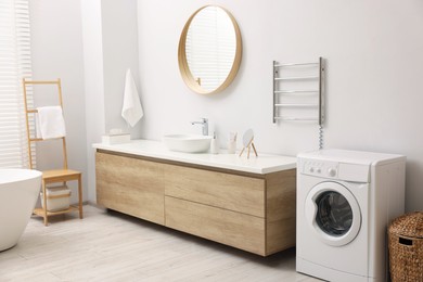 Photo of Stylish bathroom interior with heated towel rail and washing machine