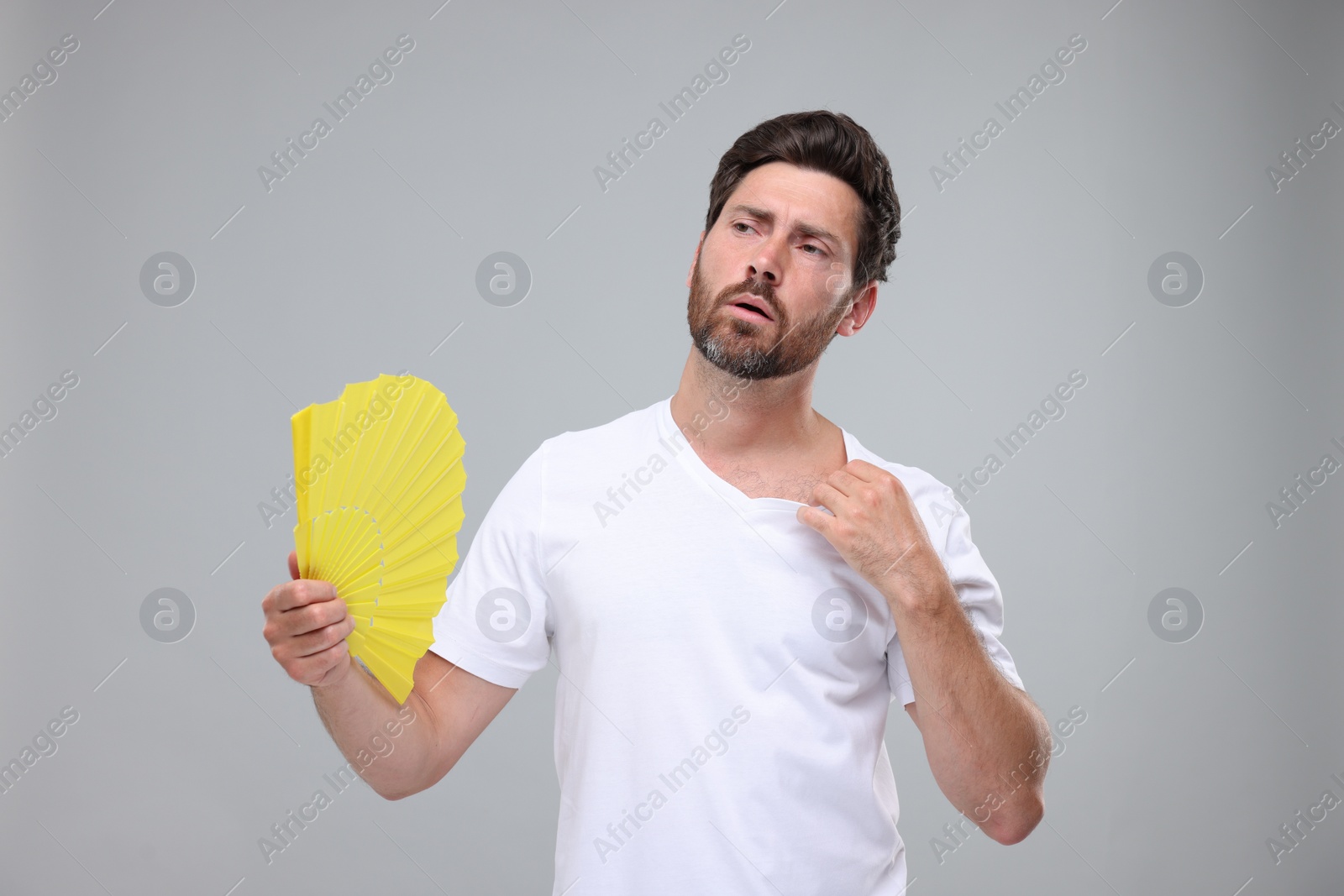 Photo of Unhappy man with hand fan suffering from heat on light grey background