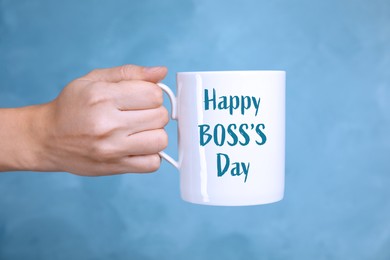 Image of Woman holding mug with phrase Happy Boss`s Day on light blue background, closeup