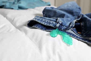 Photo of Unrolled condom and jeans on bed. Safe sex