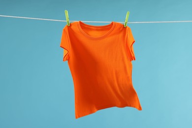 One orange t-shirt drying on washing line against light blue background