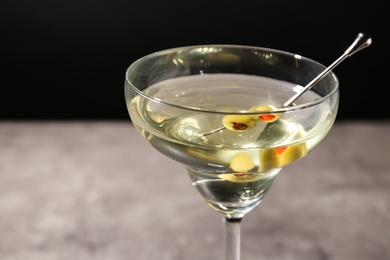 Photo of Glass of Classic Dry Martini with olives on table against black background, closeup