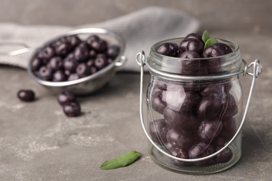 Photo of Jar of fresh acai berries on grey stone table, closeup view. Space for text