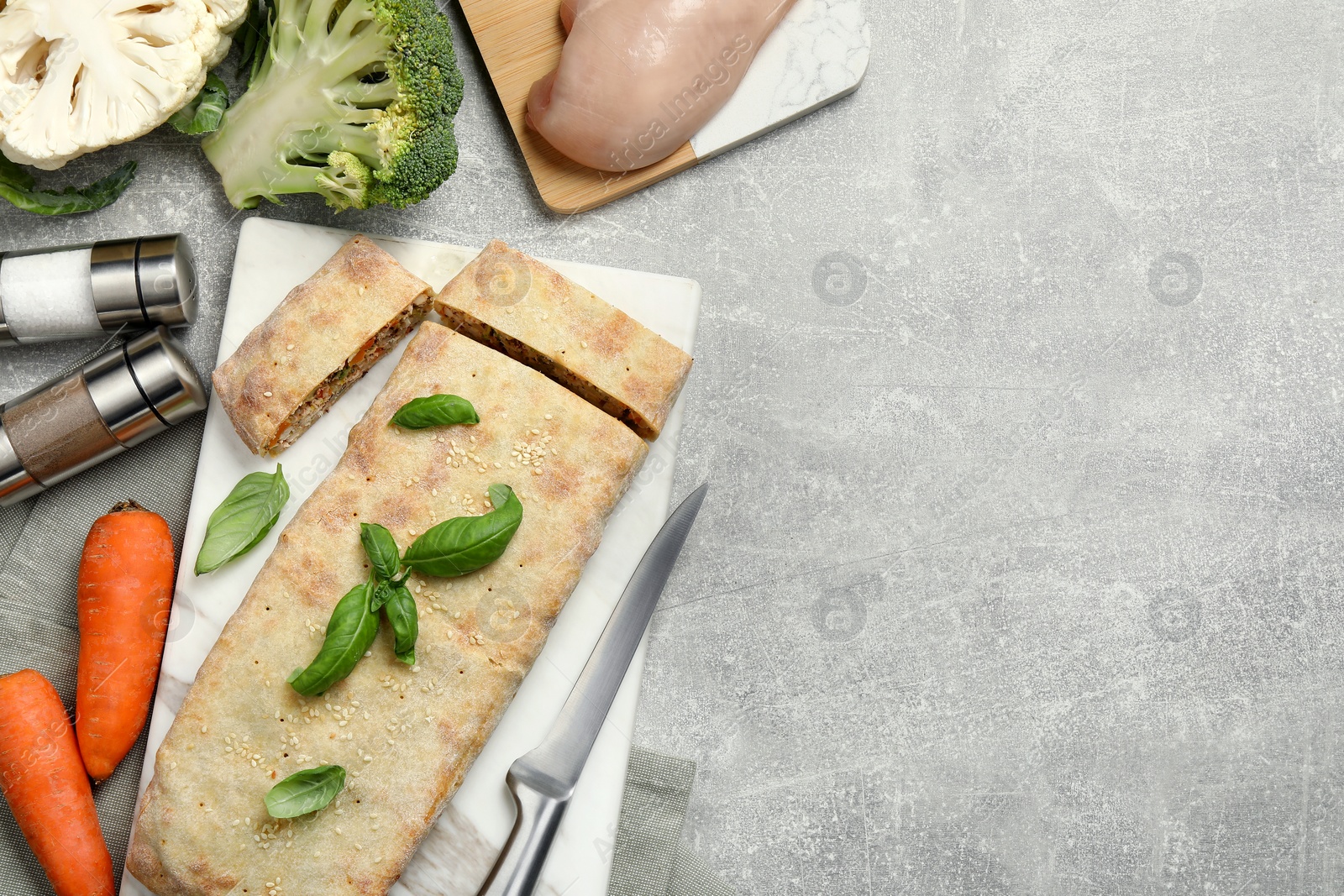 Photo of Delicious strudel with chicken, vegetables and basil served on grey table, flat lay. Space for text