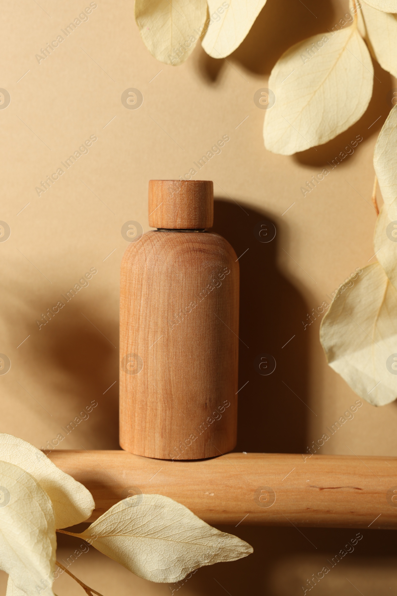 Photo of Wooden bottle of cosmetic product and dried leaves on dark beige background