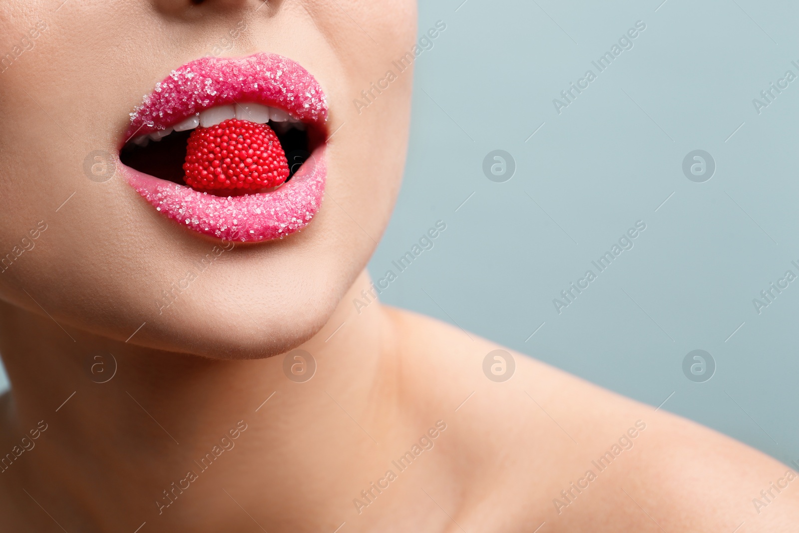 Photo of Woman with lips covered in sugar eating candy on light grey background, closeup. Space for text