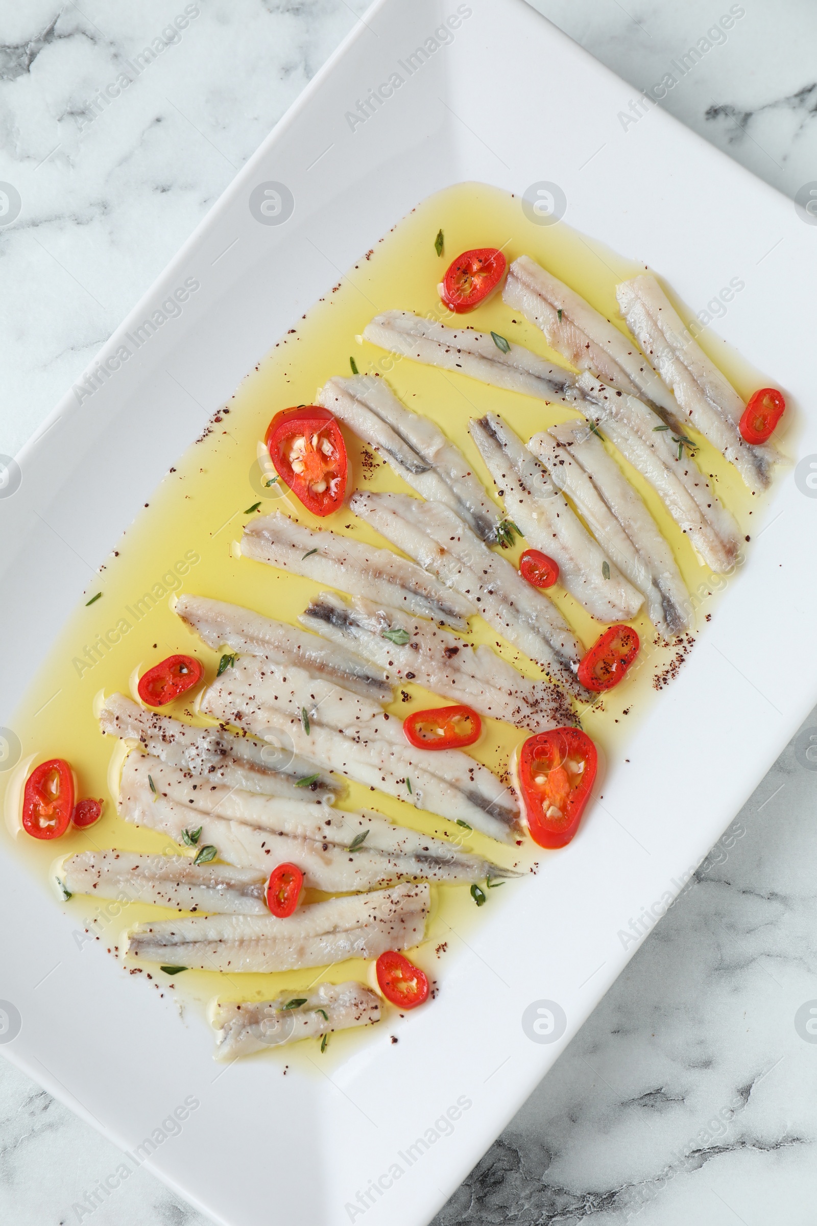 Photo of Tasty pickled anchovies with spices on white marble table, top view