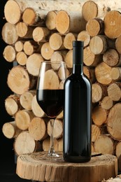 Stylish presentation of red wine in bottle and wineglass near wooden logs