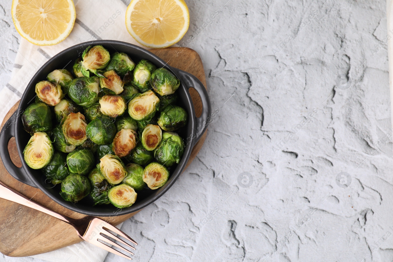 Photo of Delicious roasted Brussels sprouts in baking dish, lemon and fork on white textured table, top view. Space for text