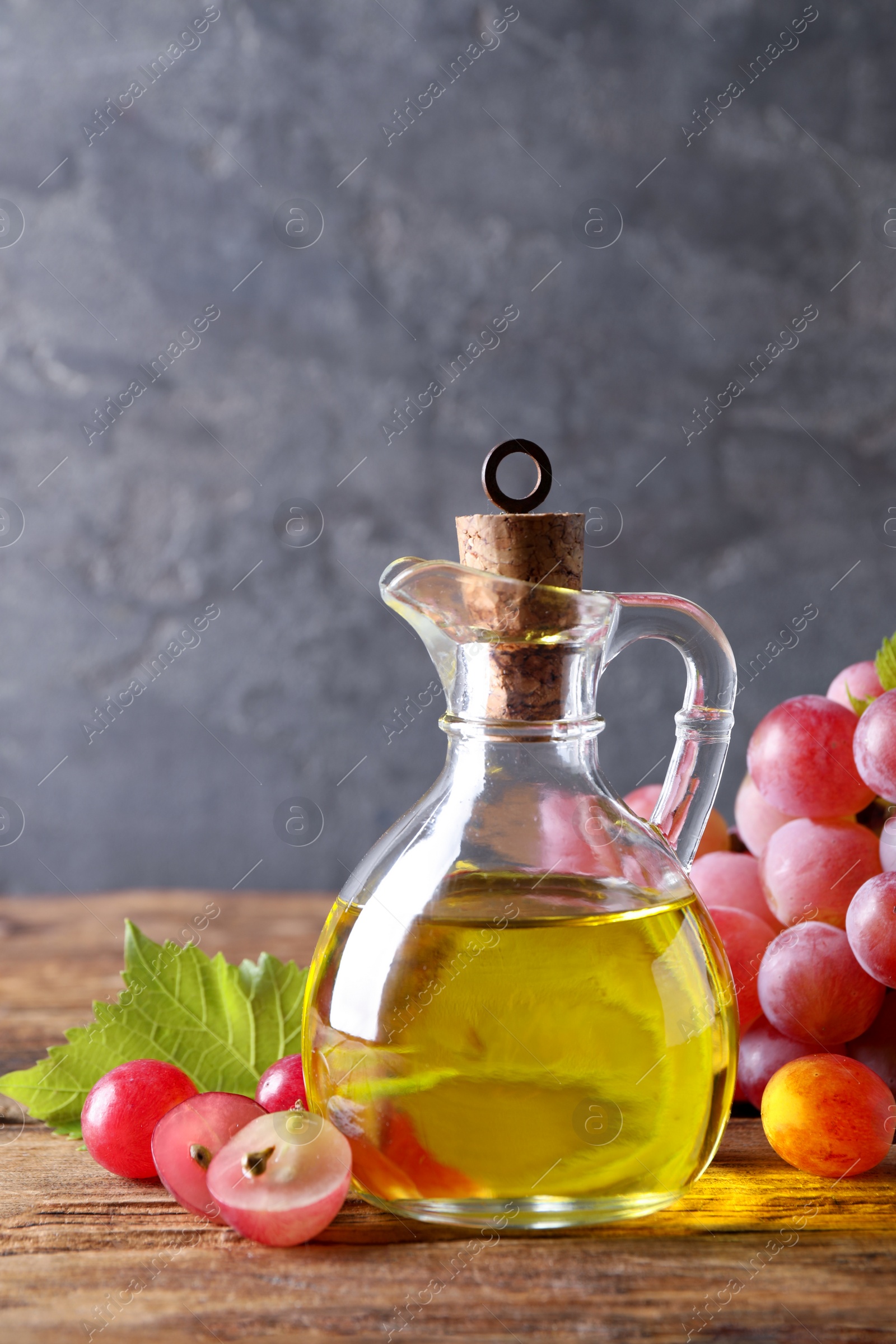 Photo of Jug of natural grape seed oil on wooden table. Organic cosmetic