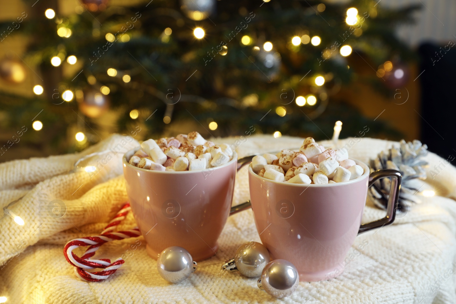 Photo of Cups of tasty cocoa with marshmallows, candy canes and Christmas decor on knitted plaid indoors