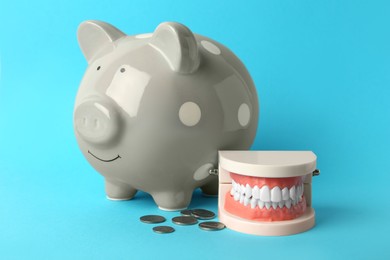 Photo of Educational dental typodont model, piggy bank and coins on light blue background. Expensive treatment
