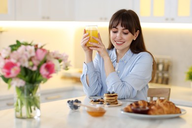 Smiling woman with glass of juice having breakfast at home