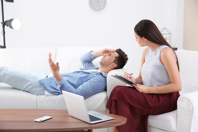 Photo of Depressed young man having appointment with psychologist in office