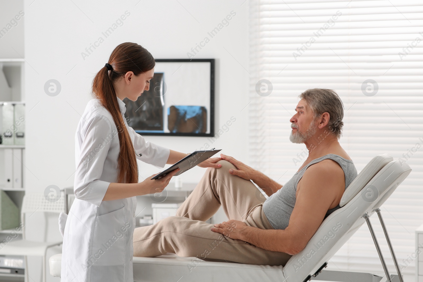 Photo of Orthopedist examining patient with injured knee in clinic