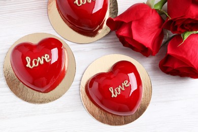 St. Valentine's Day. Delicious heart shaped cakes and roses on white wooden table, flat lay